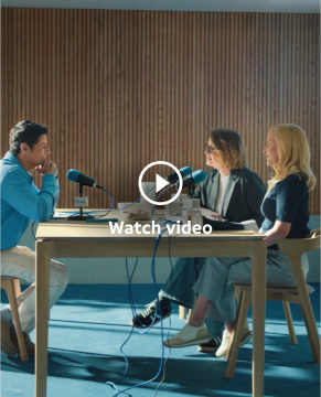 Set at a table, Jenna and Angela sit on one side while a man wearing blue sits at the other side. They each have a microphone as the an interview for a podcast takes place.